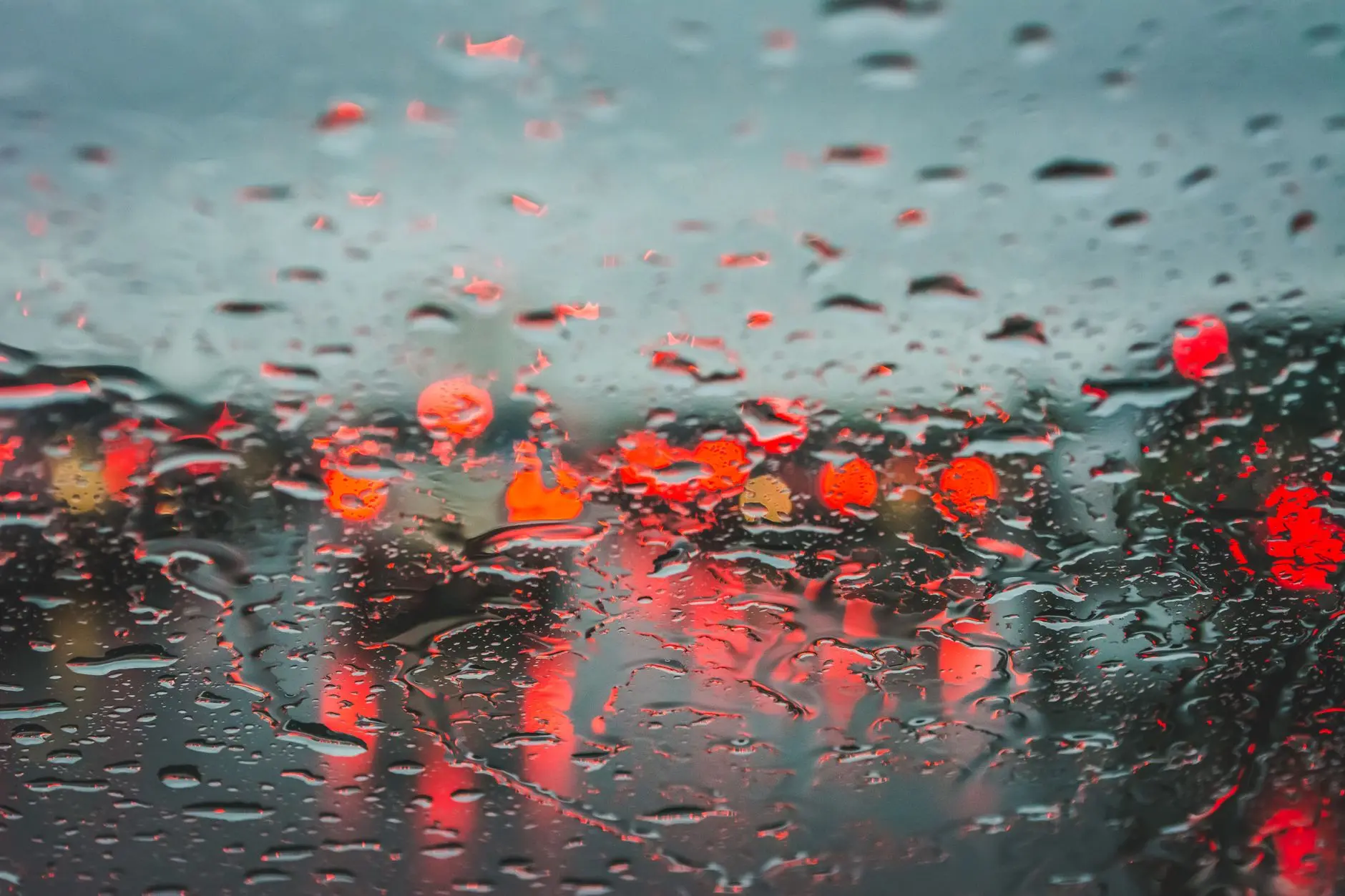 Raindrops on a window creating a blurry view with red bokeh lights shining through in Dallas.