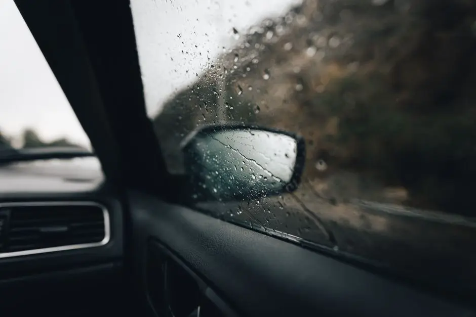 View from car interior with raindrops on window, focusing on the side mirror and road outside.