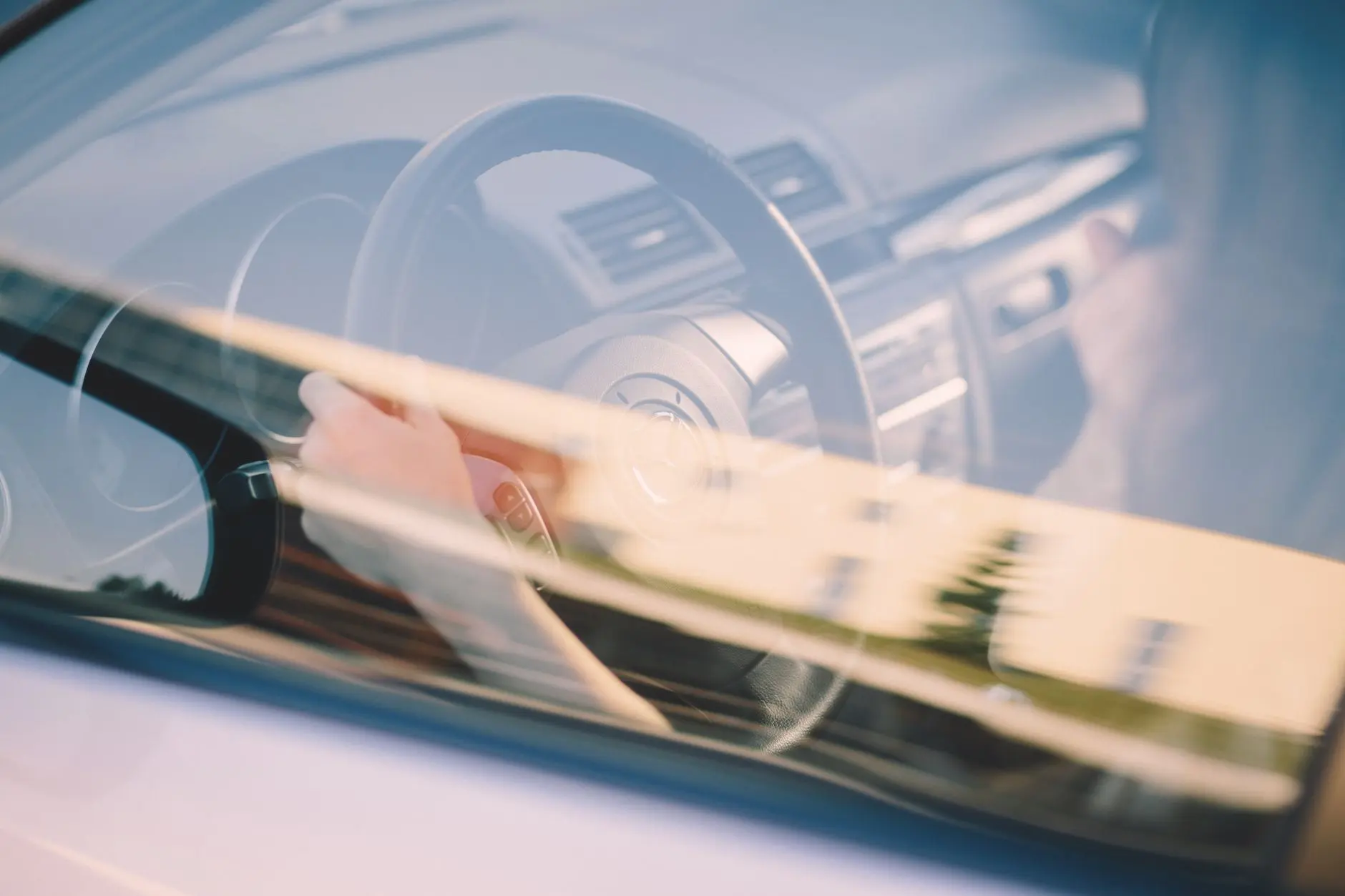 A close-up view of hands on a car steering wheel with reflections on the window.