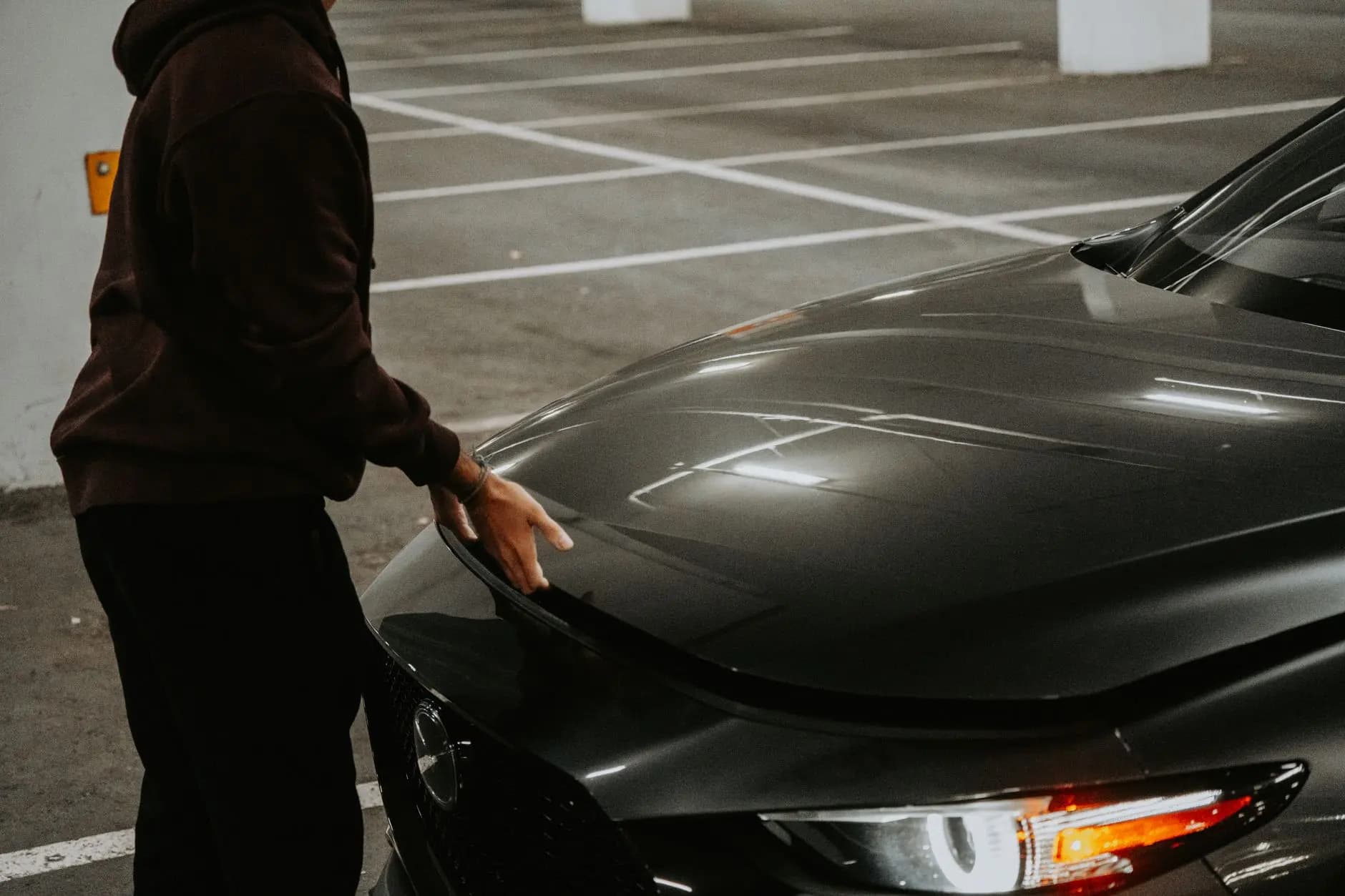 A person opens the car hood in a dimly lit parking garage, showcasing urban transportation.