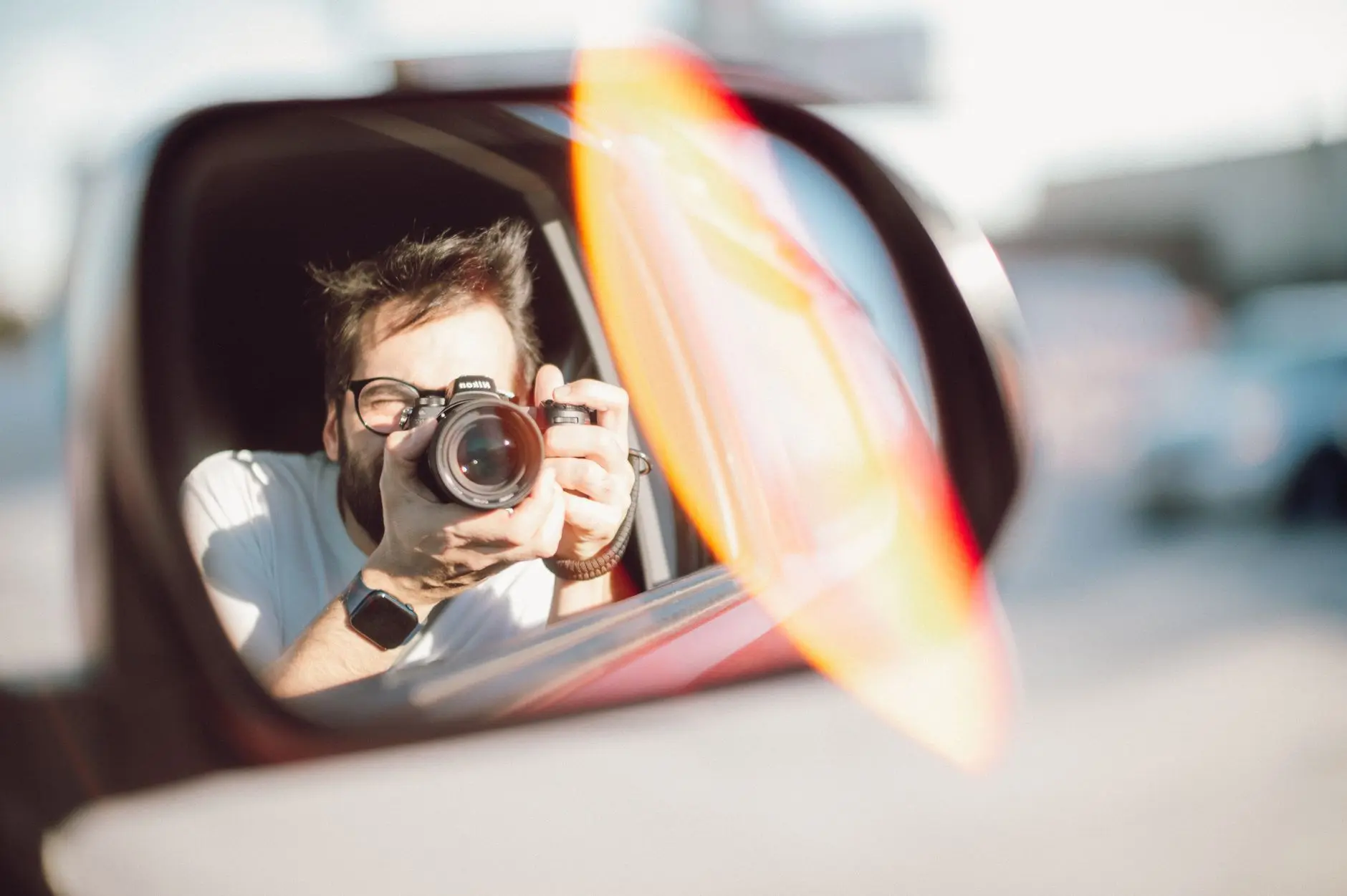 A photographer captures a candid shot through a car side mirror on a sunny day.